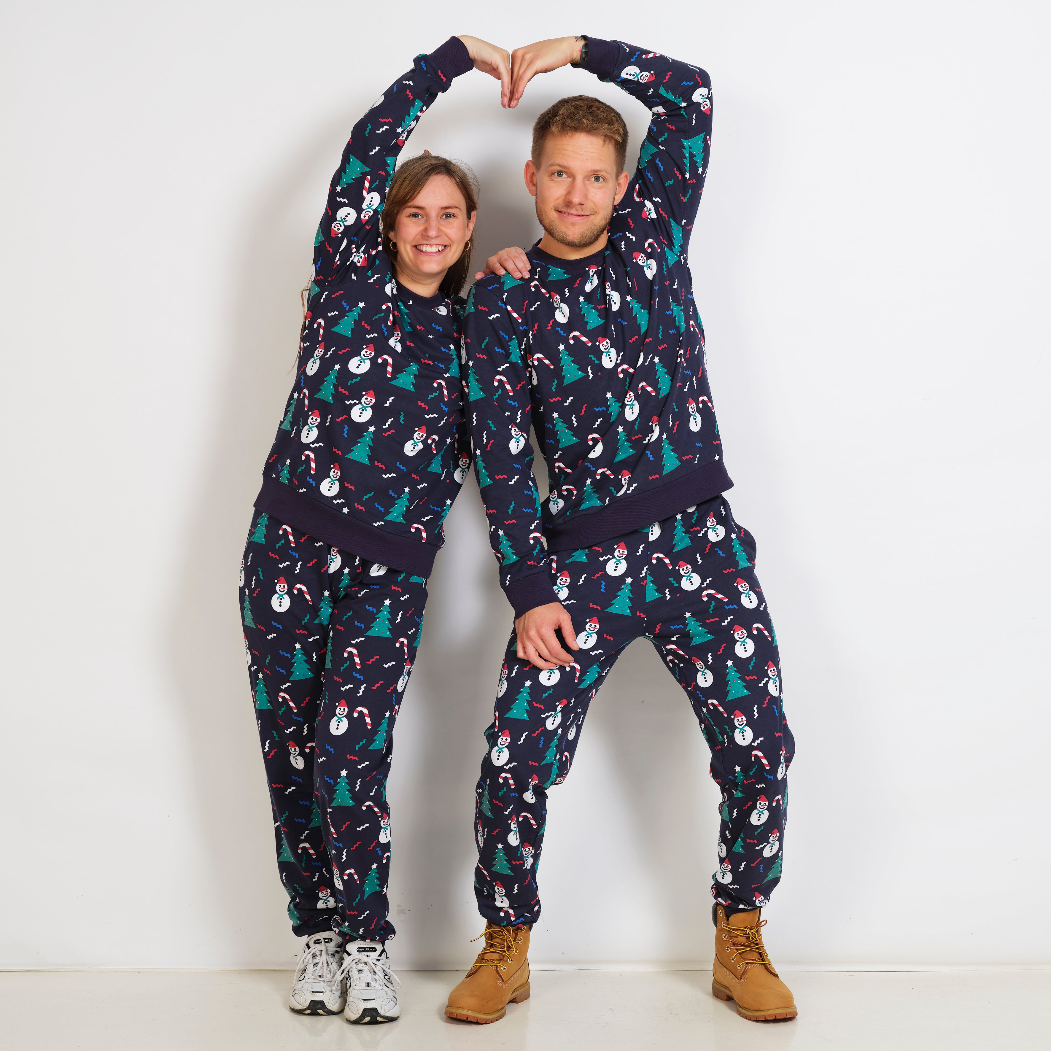 En mand og en dame poserer sammen iført et blå julesweatsuit.